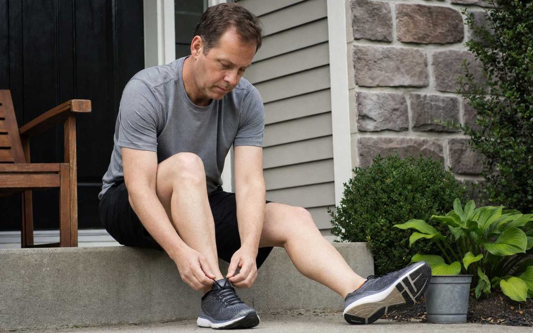 A person sitting to lace running shoes by the front door in the morning