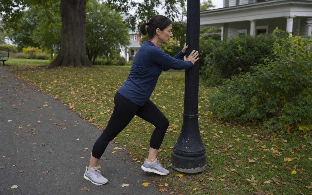 A runner pausing on a path to stretch a calf against a post