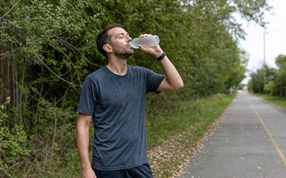 A runner drinking water from a bottle during a break on a sunny path